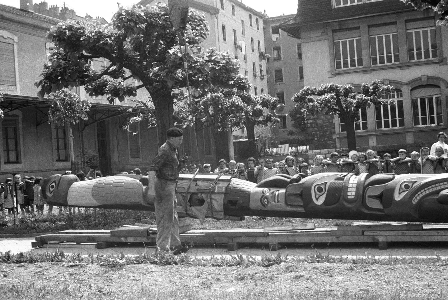 Photographie de l’arrivée des caisses et de l’installation des mâts totem dans le jardin du musée en 1956. Reproduction. Archives du MEG